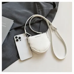 Mini sac à bandoulière blanc texture litchi à côté d'un smartphone pour comparer la taille