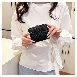 Dettaglio mini portafoglio nero trapuntato con chiusura a scatto tenuto in mano da modella