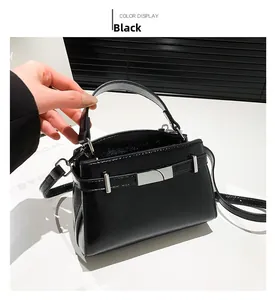 Detailed view of black glossy leather handbag with silver clasp and adjustable shoulder strap