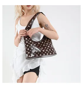 Close-up of a dark patent leather shoulder bag featuring silver metal rivets on white backdrop