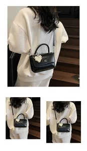 Close-up of black crossbody bag with woven handle and heart-shaped pearl charm detail