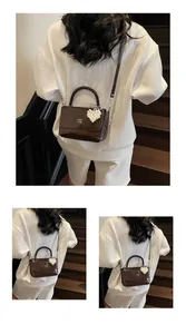 Detail of dark brown glossy handbag with woven handle and pearl heart charm accessory