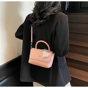 Pink crossbody bag featuring a woven handle and pearl heart charm shown on model