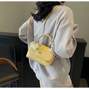 Detail of yellow glossy leather handbag with woven handle and pearl heart charm