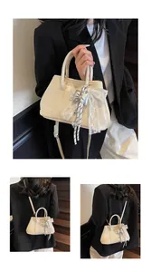 Detail of cream Boston handbag featuring decorative lace bow charm and PU leather texture