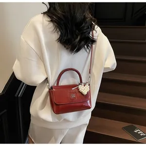 Deep red leather handbag with woven handle and pearl heart charm on a model's shoulder