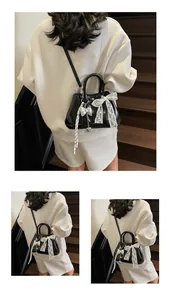 Close-up of black glossy handbag featuring white lace bow and silver heart pendant
