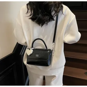 Detail of black glossy handbag with pearl heart charm and woven handle on model