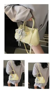 Close-up of a pale yellow lace bow pendant detail on a stylish leather handbag