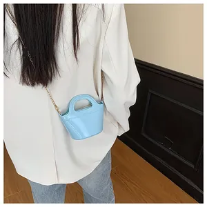 Detail of light blue patent leather mini bucket bag with gold chain strap on a white blazer