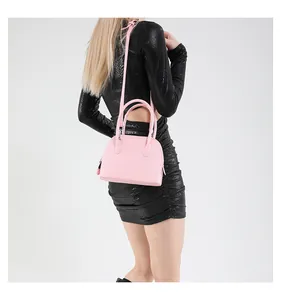 Sac coquille rose en cuir litchi porté en bandoulière sur un modèle avec sangle réglable