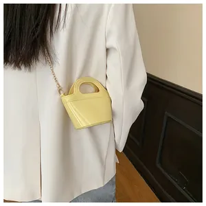 Close-up of yellow jelly bucket bag with gold chain strap on a white blazer outfit