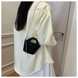 Chic black glossy mini jelly bag with gold chain strap worn over light yellow shirt