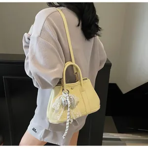 Detail of light yellow leather handbag featuring lace trim and silver bow charm accent