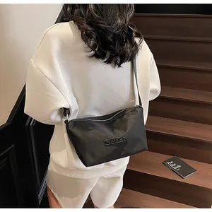 Detail of a minimalist black oxford crossbody bag with silver zipper and adjustable strap
