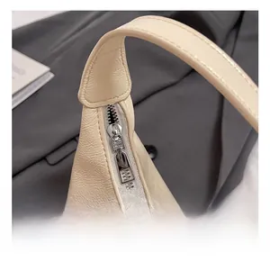Detailed macro shot of premium silver zipper and leather texture on a beige crescent bag