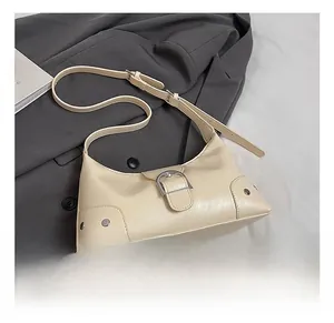 Detail view of beige leather underarm bag featuring a large silver belt buckle decoration