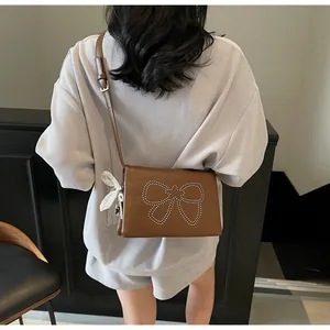 Detail of a brown crossbody bag featuring a silver rhinestone bow and a lace pearl charm