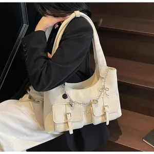 Detail of cream shoulder bag featuring double buckle pockets and silver heart chain charm