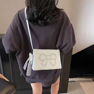 White faux leather crossbody bag with studded bow and lace ribbon on a model