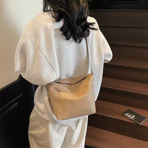 Minimalist beige oxford shoulder bag worn by model with metallic rivet details