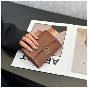 Detailed view of a brown leather tri-fold wallet with a silver metal B buckle on a magazine