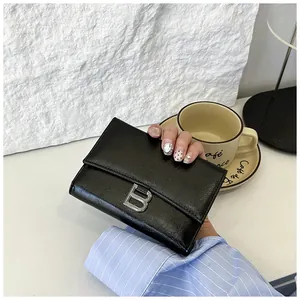 Detailed view of black leather wallet with silver B-logo held in a stylish setting