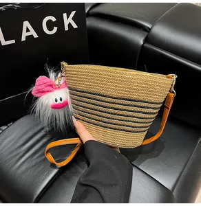 Détail du sac seau en paille avec rayures noires, bandoulière en cuir et grigri