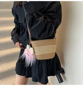 Détail du sac seau en paille tressée avec rayures blanches et charm monstre en peluche rose
