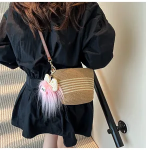 Détail du sac seau tressé avec rayures blanches et charmant pendentif en peluche rose