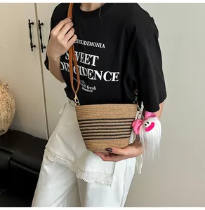 Détail du sac seau en paille tissée avec rayures noires et pendentif en peluche sur la bandoulière