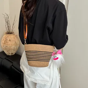 Sac seau en paille tressé avec rayures noires, bandoulière en cuir et breloque monstre