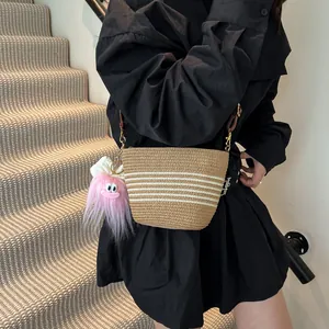 Sac seau chic en paille tissée avec rayures blanches et bandoulière en cuir marron porté