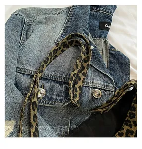 Detail of leopard print tote bag strap layered over a blue distressed denim jacket