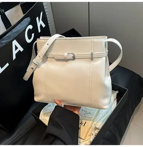 Detalle del bolso tipo cubo de piel sintética crema con costuras verticales y hebilla metal