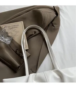 Detail der cremeweißen Leder-Tote-Bag mit dünnen Riemen auf einem stilvollen braunen Blazer