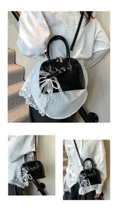 Détail du sac noir verni avec nœud en dentelle blanche et charm de perles élégantes