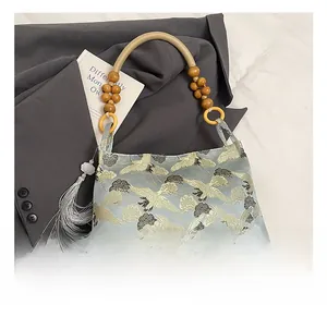 Close-up of jacquard shoulder bag featuring gold crane embroidery and wood bead handle