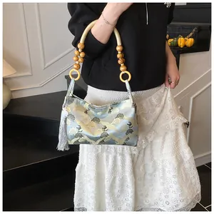 Detailed embroidery of cranes and clouds on blue satin handbag with wooden bead strap