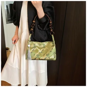 Detail of green satin handbag featuring golden crane embroidery and wooden bead handle