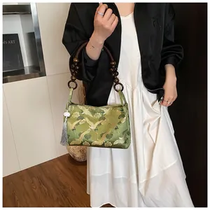 Close-up of green jacquard bag with golden crane embroidery and wooden bead handle