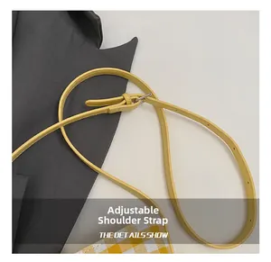 Detail of adjustable yellow leather shoulder strap with silver buckle on checkered tote bag
