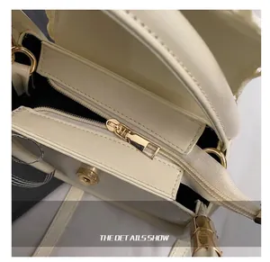 Detail of cream crossbody bag featuring polished gold hardware and smooth zipper