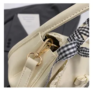 Close-up of golden metal hook hardware and gingham ribbon on the cream crossbody bag