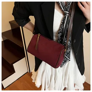Detail of burgundy velvet cylinder bag featuring long leather tassels and sleek zipper