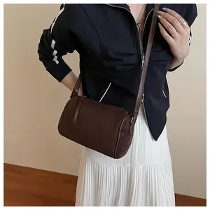 Detail of dark brown matte cylinder bag worn as a shoulder bag with a stylish outfit