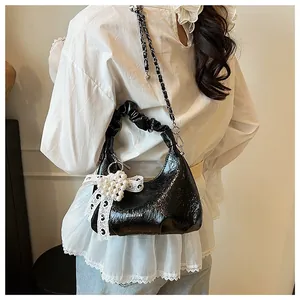 Detail of black glossy pleated shoulder bag with pearl lace bow and metal chain strap