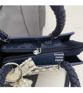 Detail of dark blue faux snake skin handbag with braided handle and pearl charm accessory