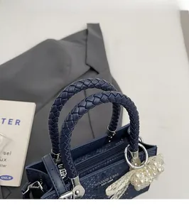 Detail of navy blue snakeskin tote with woven handle and pearl bow pendant charm