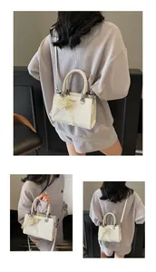 Detail of cream crossbody bag featuring braided handle and pearl heart charm accessory